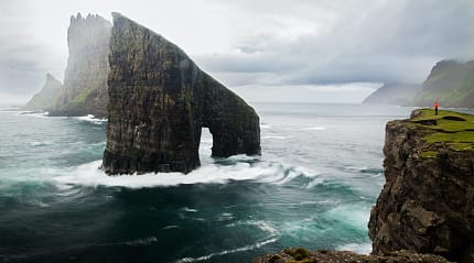 Drangarnir sea stacks rising from the Atlantic Ocean near Vágar, Faroe Islands, with dramatic cliffs and waves crashing below.