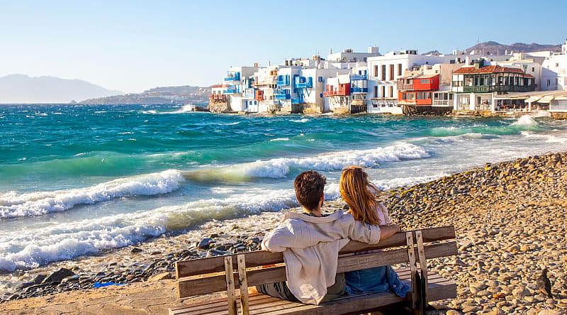 Mykonos, Greece Romantic couple sitting on a beach bench near Little Venice in Mykonos, Greece