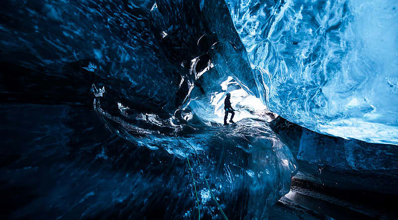 Mountain climber standing inside ice cave glacier Mountain climber standing inside ice cave glacier