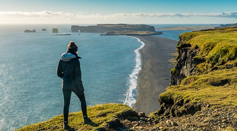 Hiker enjoying view of Reynisfjara and Dyrholaey Hiker enjoying view of Reynisfjara black sand beach and Dyrholaey in the distance