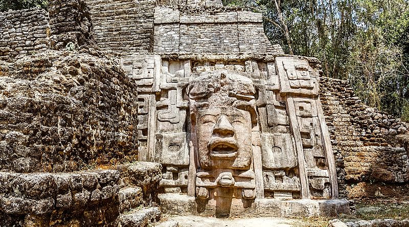 Ancient stone Mayan pre-columbian civilization pyramid with carved face in the forest, Lamanai archeological site, Orange Walk District, Belize Ancient stone Mayan pre-columbian civilization pyramid with carved face in the forest, Lamanai archeological site, Orange Walk District, Belize