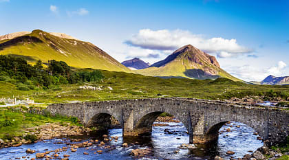 Old vintage brick bridge crossing river in Sligachan, Isle of Skye, Scotland with blue sky, hills and mountains in the background