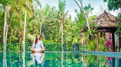 Woman meditating poolside at luxury resort in Bali