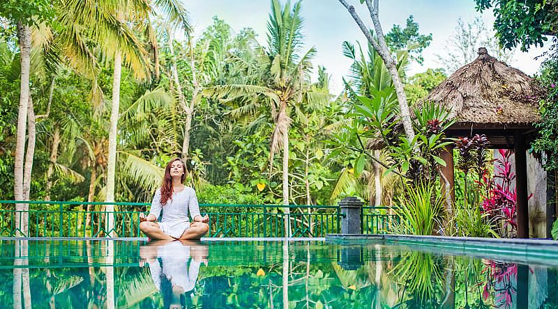 Woman meditating poolside at luxury resort in Bali