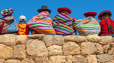 Native Peruvian women pose on a rock wall with a young tourist in Cusco