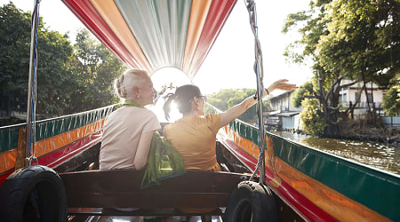 Senior travelers riding a colorful longtail boat through a canal at sunset in Bangkok, Thailand