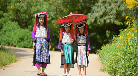 Three young Lahu Tribe girls in custom dress, smiling among the sunlight in Thailand.