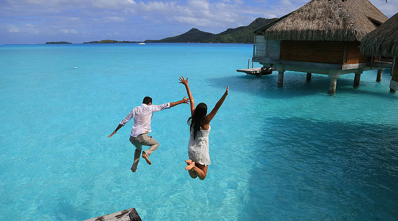Happy young couple jump into the water from their over water bungalow in Bora Bora