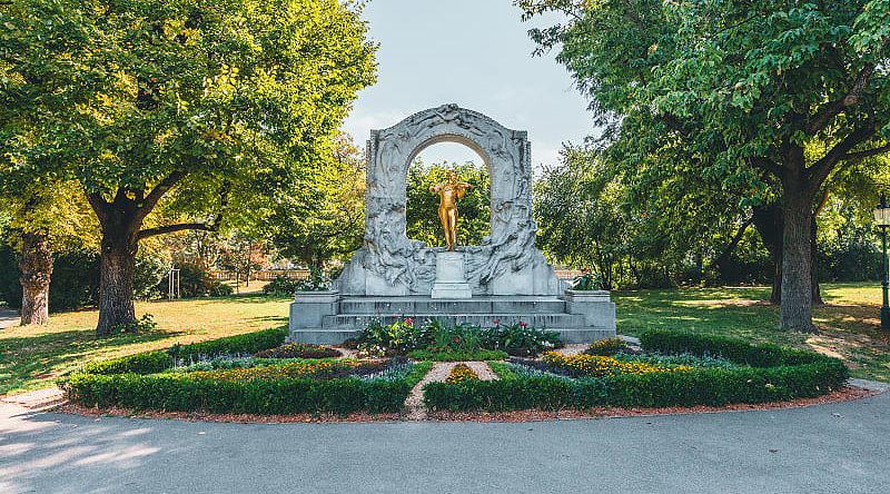 Golden Johann Strauss statue in Stadtpark, Vienna, surrounded by trees and a beautiful garden setting