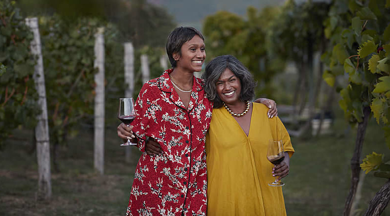 Smiling mother and daughter holding wineglasses and standing with arms around each other at a vineyard