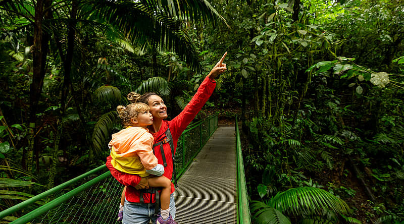 "Mother and child on a rainforest walkway in Arenal, Costa Rica, exploring and pointing at the lush greenery.