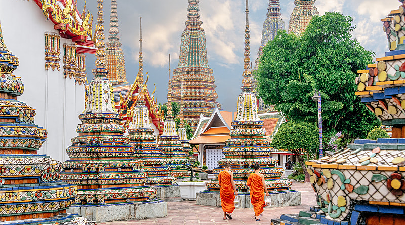 Two monks in colorful orange robes walking through Wat Pho Temple in Bangkok, Thailand