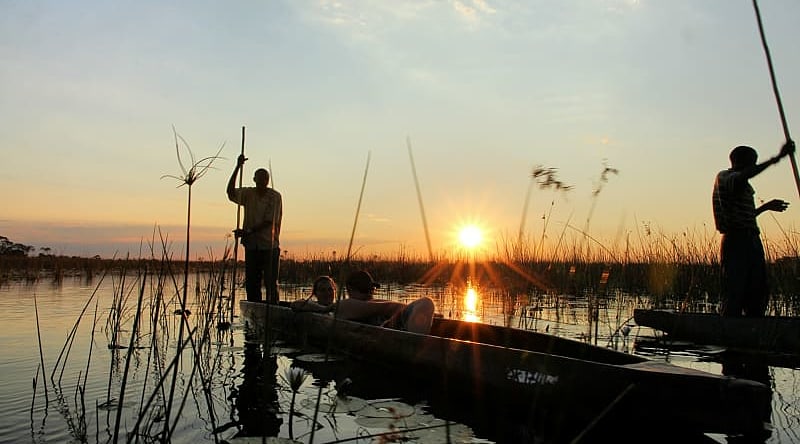 Couple on mokoro boat safari at sunset in the Okavango Delta, Botswana