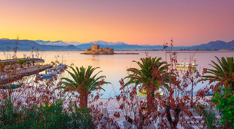 Nafplio Greece with palm trees, boats and Bourtzi castle on the water at sunset