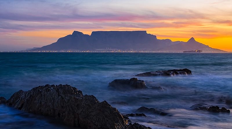 Silhouette of Table Mountain against sunset sky and ocean waves in Cape Town, South Africa