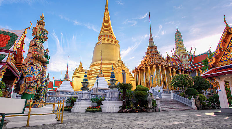Grand Palace in Bangkok with golden stupa and ornate temples in Wat Phra Kaew at sunset.