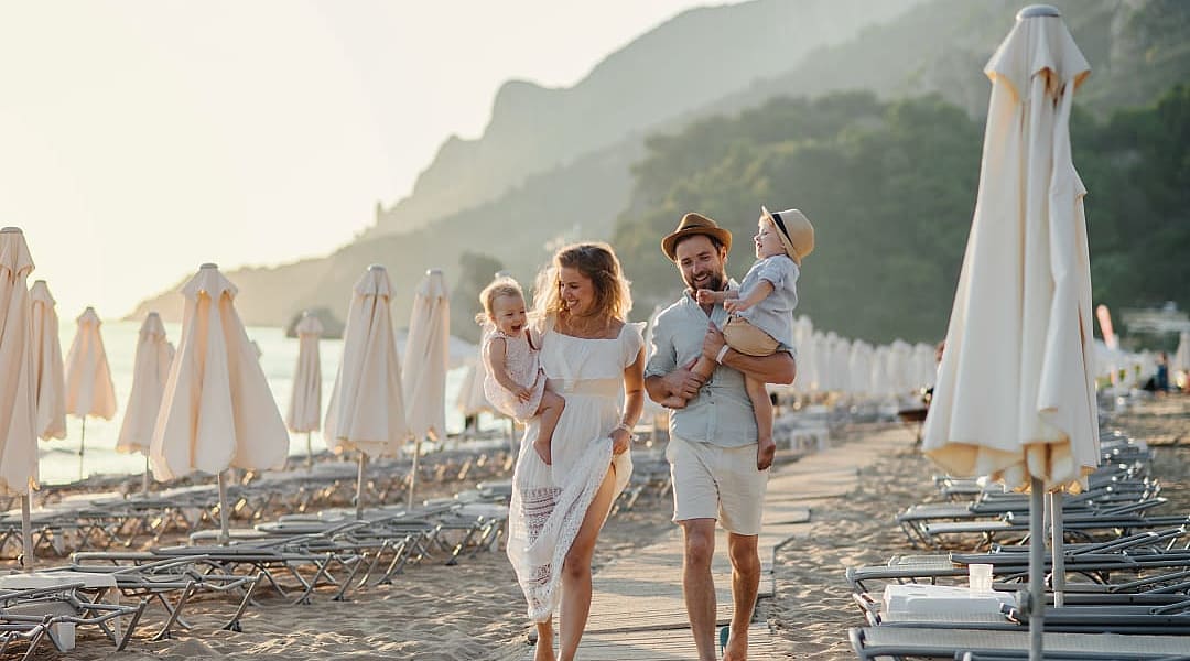 A young family with two toddler children walking on beach on summer vacation