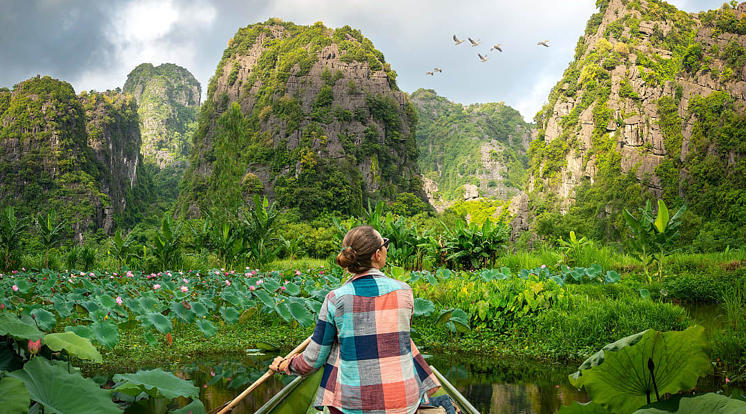 woman travels along river in boat, enjoying picturesque karst mountains in Ninh Binh Province, Vietnam