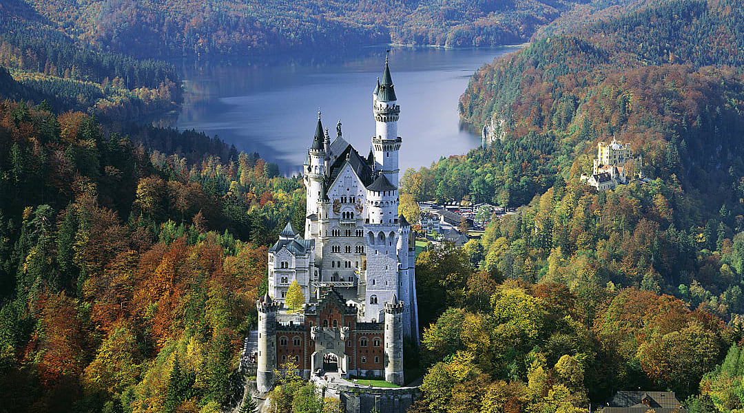 Neuschwanstein Castle in Bavaria, Germany, surrounded by autumn forest and overlooking a mountain lake