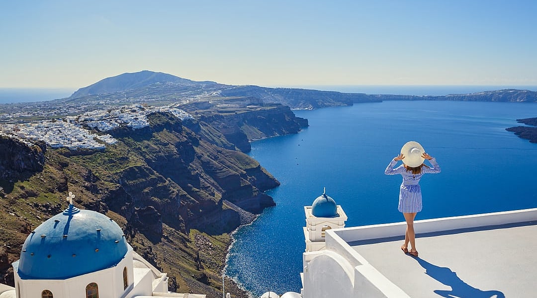 A woman admires Santorini’s breathtaking caldera and deep blue Aegean Sea.
