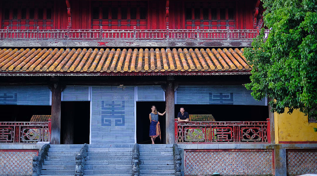 Travelers at the Imperial City of Hue, Vietnam, standing outside a historic temple with red columns and tiled roof.