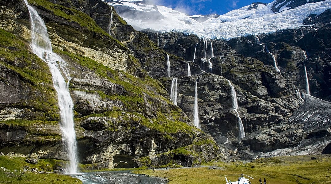 Couple heli hiking at Earnslaw Burn with hanging glacier and cascading waterfalls