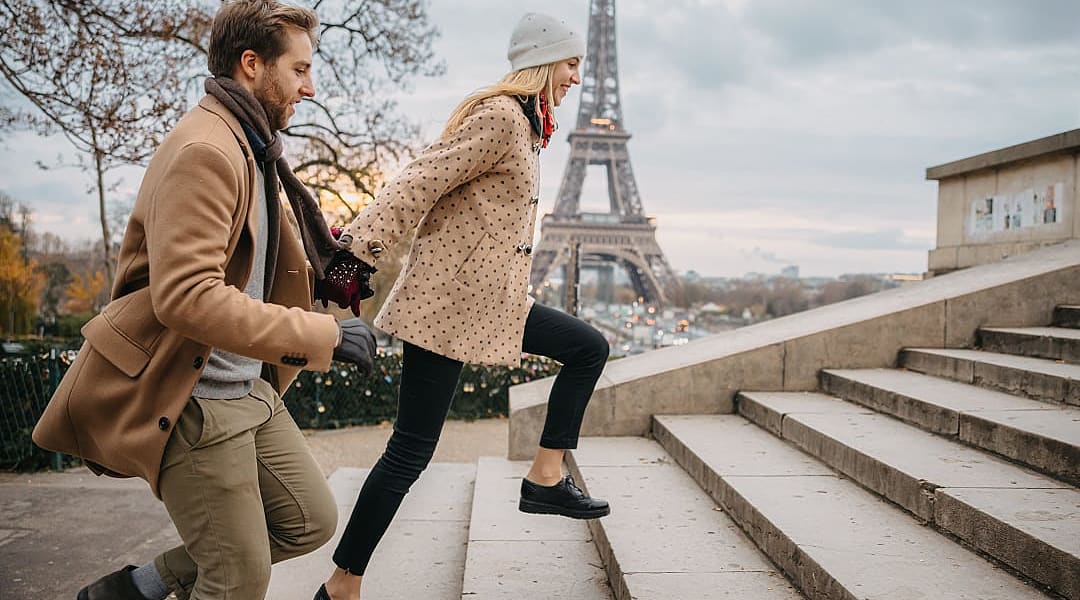 Romantic couple standing in front of the Eiffel Tower in Paris, France, under a cloudy sky, with the iconic monument towering in the background