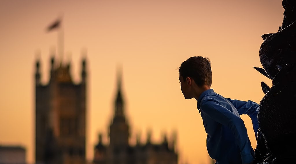 Child climbing a lamp post in south bank in london (uk) at sunset with the houses of parliament in the background