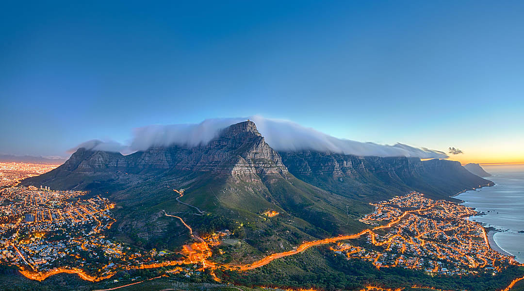 Stunning aerial view of Table Mountain, Cape Town, at sunset with city lights and clouds over the peak