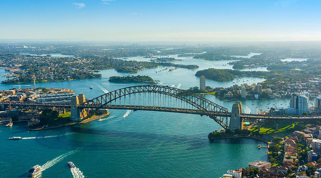 Sydney’s Harbour Bridge stretches proudly across sparkling, boat-filled waters.
