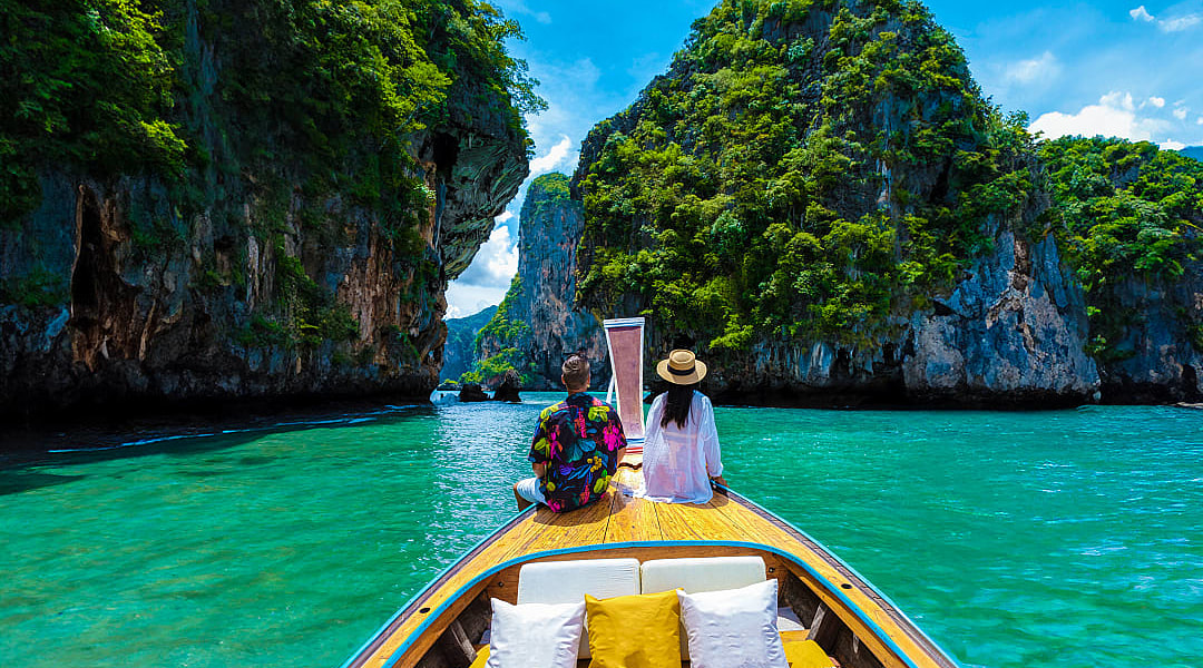 Couple on a traditional boat exploring turquoise waters and limestone cliffs in Krabi, Thailand
