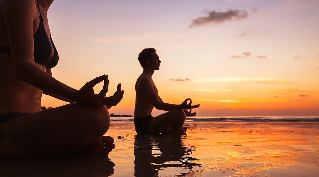 A couple practicing some meditation during a sunrise in French Polynesia.
