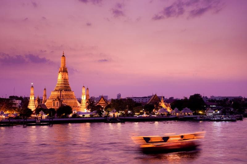 a boat sails down a river with a pagoda in the background at twilight in Wat Arun