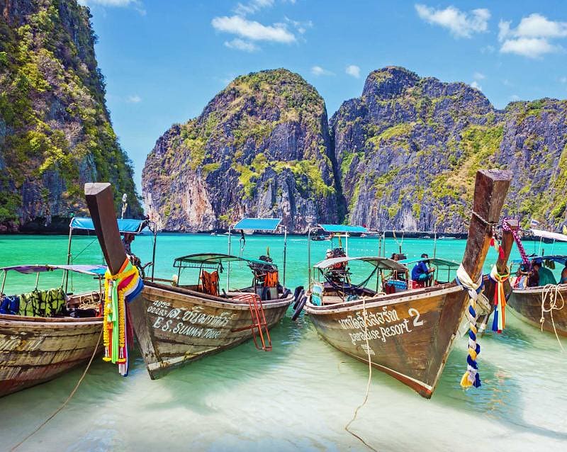 Wooden boats in the turquoise waters of Maya Bay with limestone karst cliffs on Phi Phi island in Thailand