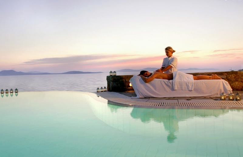 Woman masseuse giving a woman customer a massage poolside at the Mykonos Grand Hotel & Resort