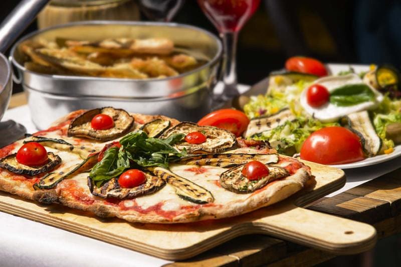 Freshly made Italian pizza with eggplant, tomato and basil | Salad and garlic bread in the background