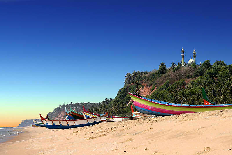 Colorful boats in front of Varkala South Cliff with mosque on top in Kerala, India.