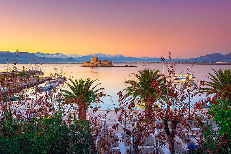 Nafplio Greece with palm trees, boats and Bourtzi castle on the water at sunset