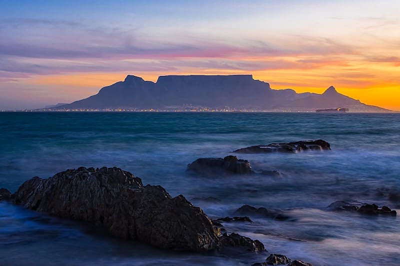 Silhouette of Table Mountain against sunset sky and ocean waves in Cape Town, South Africa