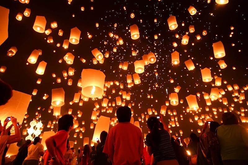 Large group of people releasing lit lanterns into sky during floating lantern festival in Thailand