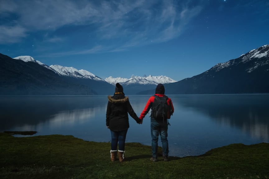 Couple holding hands standing on lake looking the night starry sky and mountain reflection in Patagonia Argentina