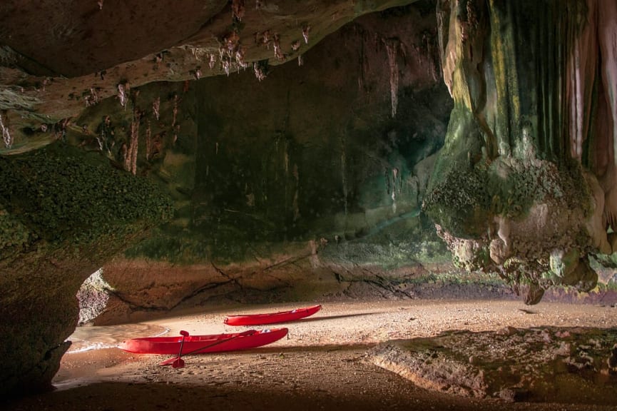 Two red kayaks on the sand at the entrance to a cave in Koh Lanta, Thailand