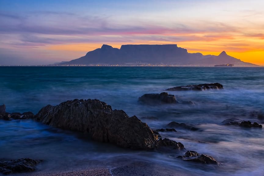 Silhouette of Table Mountain against sunset sky and ocean waves in Cape Town, South Africa