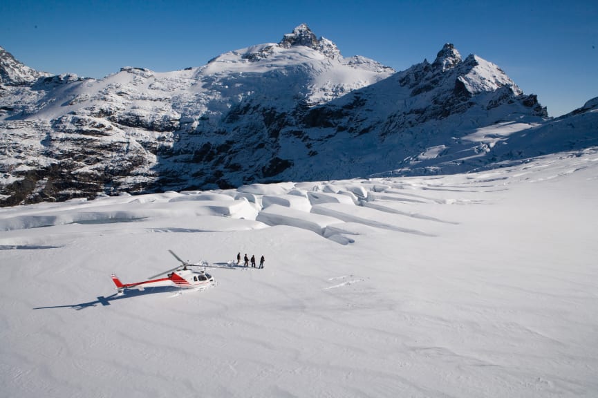 Group of travelers standing near a helicopter on Clarke Glacier in New Zealand 