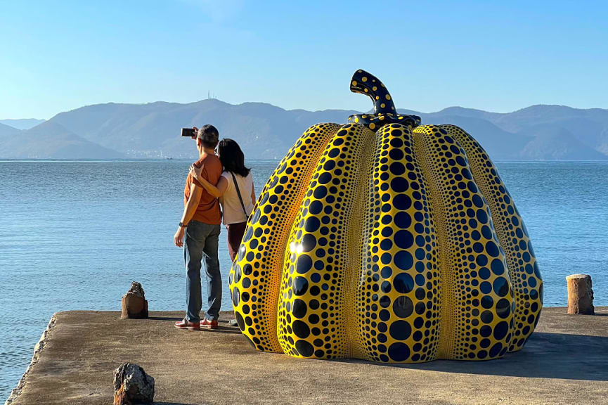 Couple in front of Yayoi Kusama’s famous and whimsical pumpkin sculpture on Naoshima Island, Japan