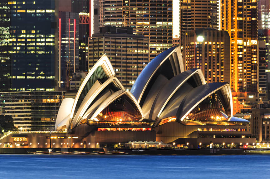 Sydney Opera House with high rise buildings at night in Australia.