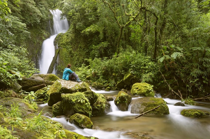 Hiking woman sitting on a stone in front of a beautiful waterfall