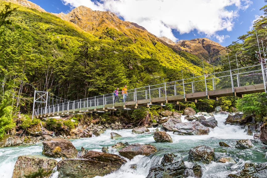 Hiking couple crossing river bridge along the Routeburn Track in New Zealand