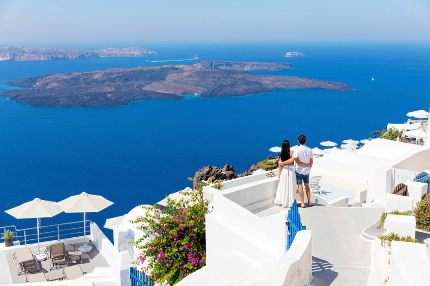 Couple standing on whitewashed balcony enjoying the view on Santorini, Greece