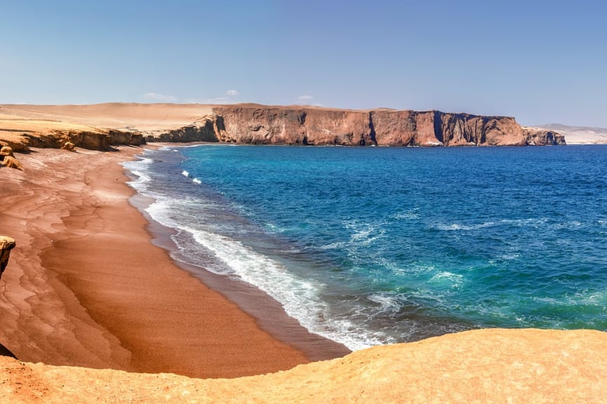 Clear blue waters and craggy coastline of La Mina Beach in Paracas National Reserve, Peru